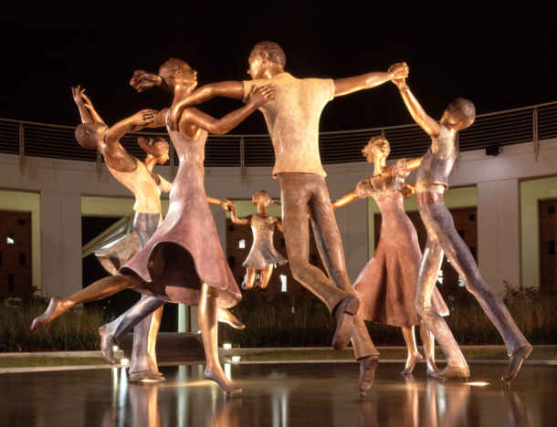 <p>When commissioned to create an artistic centerpiece for the Mattie Kelly Arts Center, internationally famous sculptor Esther Wertheimer worked in the small Italian community of Pietrasanta for 18 months to produce this inspiring sculpture.</p>
<p>Entitled the Seven Dancers, this nine-foot, bronze sculpture graces the central courtyard of the Mattie Kelly Arts Center, known as the circus.</p>
<p>The sculpture depicts seven dancers - three men, three women and a child - who hold hands to form a circle as they dance, floating above a gently overflowing pool of water. The circle they form is a symbol of never-ending camaraderie and a new hope for peace and harmony. Since the sculpture was installed in 1997, Wertheimer's work has become an icon of the complex.</p> Mattie Kelly Arts Center Seven Dancers Sculpture